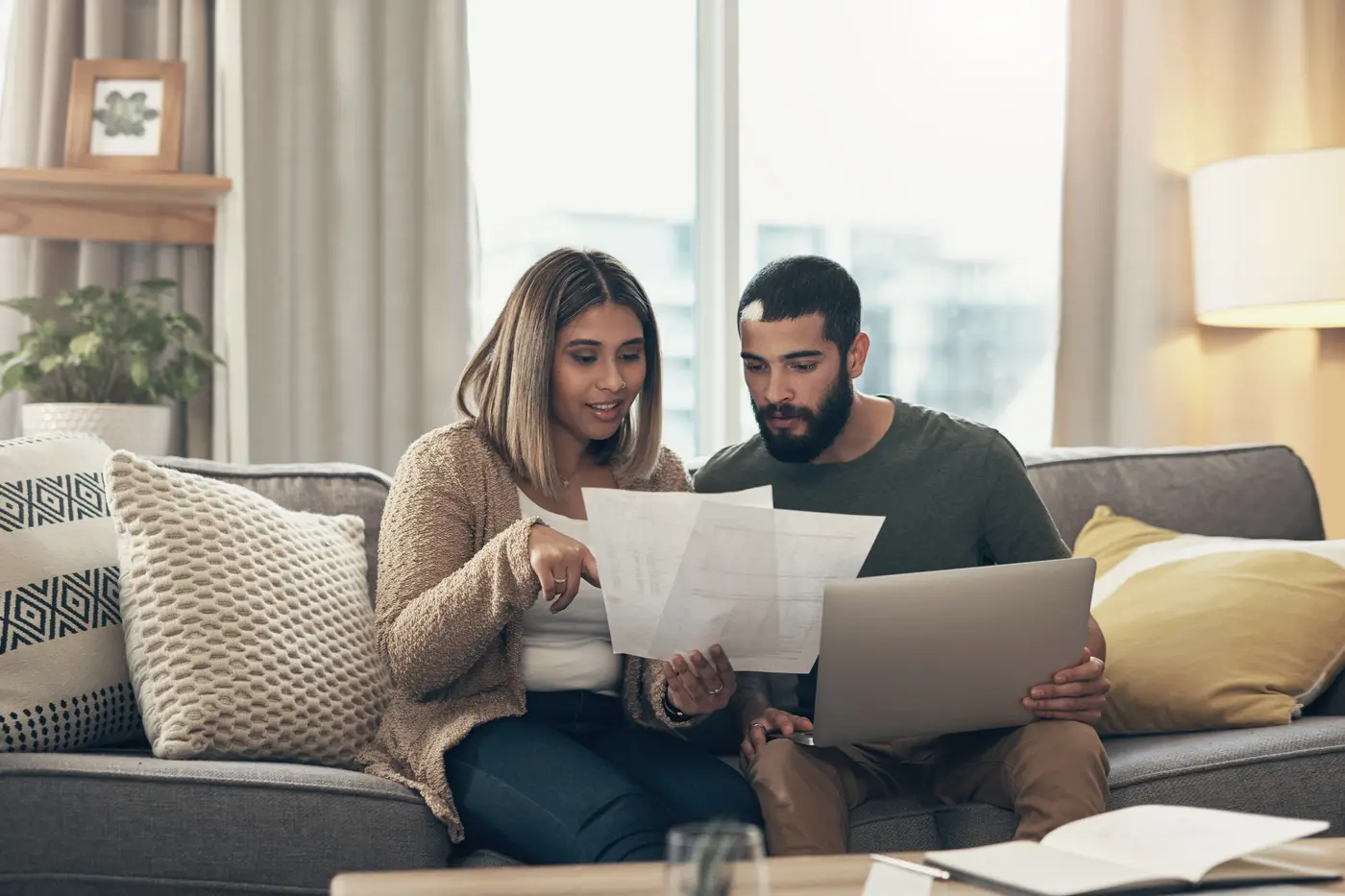 Een man en een vrouw op de bank bekijken samen een document, met een laptop op schoot